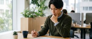 オフィスのデスクで書類を見ながら転職を思案する若い男性